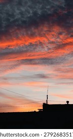 Dramatic sunset sky filled with dark grey altocumulus clouds illuminated by vibrant orange and red sunlight from beneath.