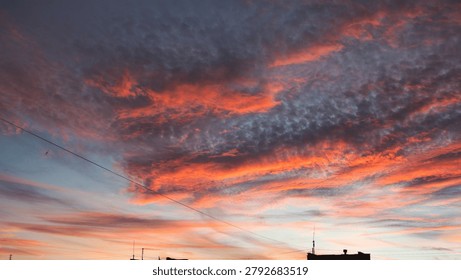 Dramatic sunset sky filled with dark grey altocumulus clouds illuminated by vibrant orange and red sunlight from beneath.