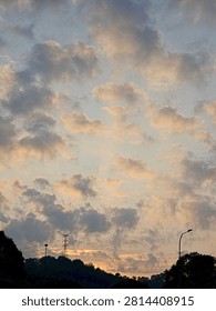 Dramatic sunset sky with glowing clouds above silhouetted trees, power lines, and streetlights, capturing a calm evening atmosphere.