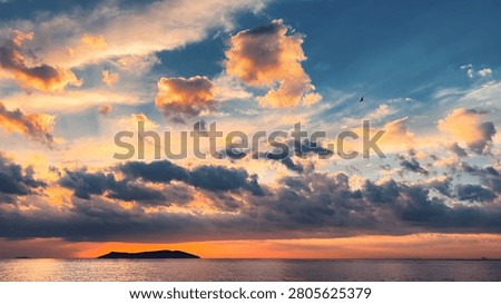 Dramatic sunset sky with golden and orange clouds over Marmara Sea with island silhouette on horizon and seagull in flight