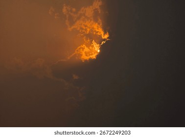  Dramatic sunset sky hidden behind clouds

 A fiery golden-orange sun partially hidden behind thick dark clouds, creating a dramatic lighting effect in the sky.