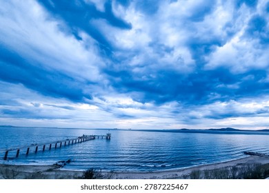 Dramatic sunset sky with intense blue clouds over the sea and a long pier stretching into the water, scenic coastal landscape, Burgas, Bulgaria.