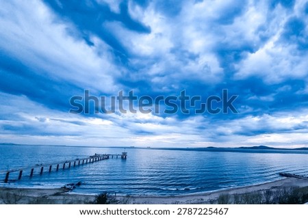 Dramatic sunset sky with intense blue clouds over the sea and a long pier stretching into the water, scenic coastal landscape, Burgas, Bulgaria.