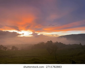 Dramatic sunset sky with orange and purple clouds over a misty mountain valley and green rolling hills.