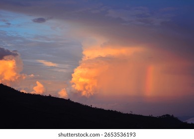 A dramatic sunset sky over a dark landscape, featuring a large, illuminated cloud formation and a subtle rainbow or light beam. Related to atmospheric phenomena, dramatic skies, tranquility of dusk