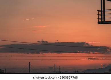 Dramatic sunset sky over distant mountains and city silhouette layered with electrical power lines and overhead wires, Japan.