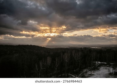 Dramatic sunset sky over landscape with sun rays breaking through clouds above forest and distant city