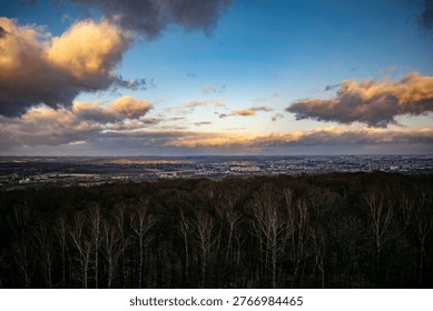 Dramatic sunset sky over landscape with sun rays breaking through clouds above forest and distant city