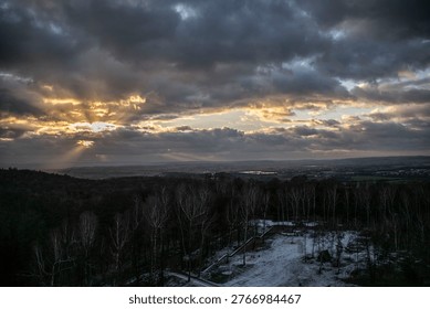 Dramatic sunset sky over landscape with sun rays breaking through clouds above forest and distant city