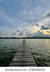 Dramatic sunset sky over a long wooden pier stretching into the calm sea, tropical landscape.