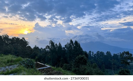 Dramatic sunset sky over Mount Merbabu area in Central Java, Indonesia, featuring colorful twilight clouds and silhouetted trees along the highland horizon.