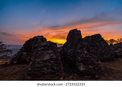 Dramatic Sunset Sky Over Rugged Mountain Rock Formations
A breathtaking view of large, dark rock formations silhouetted against a vibrant and dramatic sunset or sunrise sky, featuring warm orange, yellow, and deep blue colors