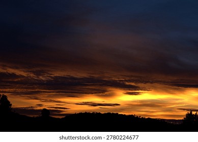 Dramatic sunset sky over silhouetted hills. Dark dramatic clouds illuminated by warm sunset light over silhouetted hills and landscape at dusk.


