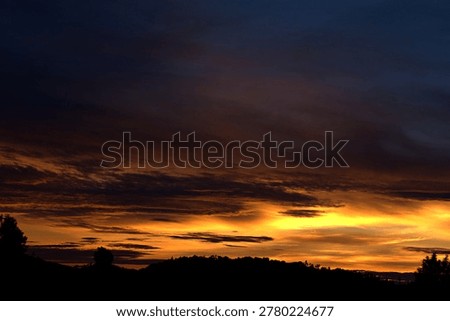 Dramatic sunset sky over silhouetted hills. Dark dramatic clouds illuminated by warm sunset light over silhouetted hills and landscape at dusk.

