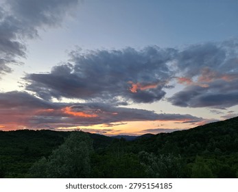 Dramatic sunset sky with pink and orange light reflecting on dark clouds over green hills.