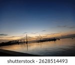 Dramatic sunset sky with red clouds over a distant bridge and calm sea
