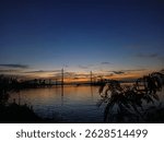 Dramatic sunset sky with red clouds over a distant bridge and calm sea
