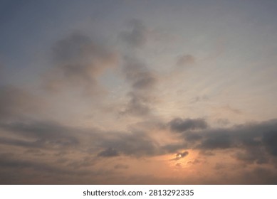 Dramatic sunset sky with soft pink and orange light breaking through dark clouds. Atmospheric cloudscape. Weather, nature, climate, and scenic background concept