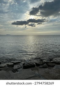 Dramatic sunset sky with sun rays shining through clouds over the sea and rocky shore