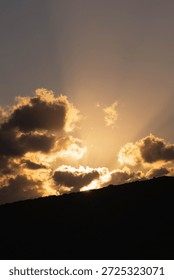 Dramatic sunset with sun rays breaking through dark clouds over mountain silhouette, Crete Greece. Golden light Mediterranean evening sky.