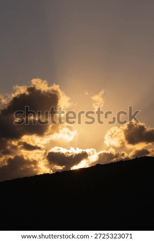 Dramatic sunset with sun rays breaking through dark clouds over mountain silhouette, Crete Greece. Golden light Mediterranean evening sky.