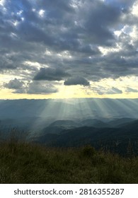 Dramatic sunset with sunbeams breaking through stormy clouds over layered mountain ranges in Thailand