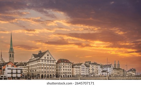 Dramatic sunset with vibrant orange clouds over the historic Old Town (Altstadt) of Zurich, featuring the Fraumünster church and iconic buildings along the Limmat river in Switzerland