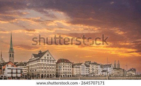 Dramatic sunset with vibrant orange clouds over the historic Old Town (Altstadt) of Zurich, featuring the Fraumünster church and iconic buildings along the Limmat river in Switzerland