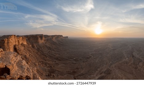Dramatic sunset view from the Edge of the World near Riyadh, with sheer sandstone cliffs dropping into vast desert plains under streaked skies.