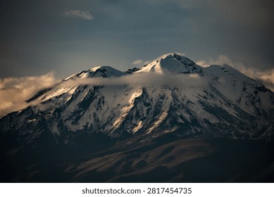 Dramatic sunset view over a massive snow-capped volcanic mountain peak in golden light