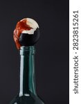 Dramatic surreal studio still life of a cracked black painted egg with orange yolk balanced on a wine bottle neck against a dark background. The cracked egg revealing its interior while perched on the bottle creates a powerful symbolic conceptual image. Suitable for Halloween editorial, surreal concept advertising, fine art photography, Easter content with a dark aesthetic, wine brand advertising, and art direction requiring unusual symbolic imagery. No people, dark studio background.