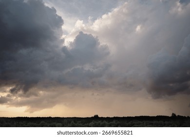 Dramatic thunderous sunset sky with dark huge rain clouds over green forest