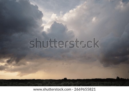 Dramatic thunderous sunset sky with dark huge rain clouds over green forest