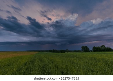 Dramatic thunderstorm clouds and lightning strike over green fields in Masuria, Poland during summer evening.
