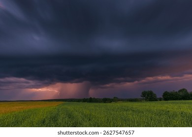 Dramatic thunderstorm with visible lightning and dark clouds over green fields in Masuria, Poland at dusk.