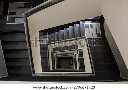 Dramatic top down view looking into the square spiral core of a modernist tenement building staircase, creating a geometric vertigo effect.