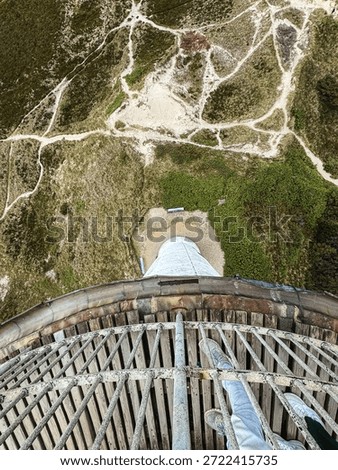 dramatic top-down view from lighthouse balcony over winding sandy paths and coastal vegetation. perspective, height and adventure, unique viewpoint of rugged shoreline terrain.