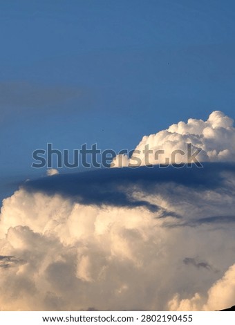 Dramatic towering Cumulus Congestus clouds with rare accessory Pileus cloud formation on top against a bright blue sky.