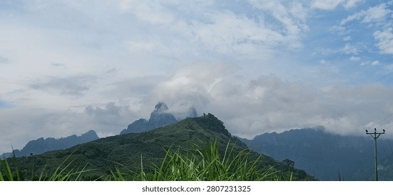 Dramatic tropical landscape of sharp limestone karst mountain peaks shrouded in thick white fog and low clouds behind green hills in Binh An, Tuyen Quang province, Vietnam.