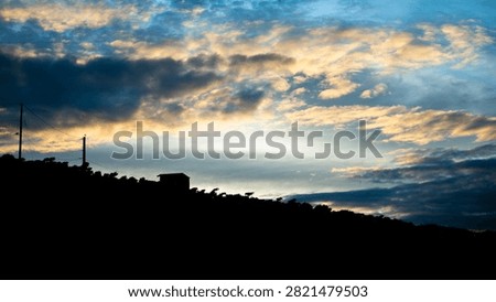 Dramatic twilight cloudscape over dark hill and house silhouette