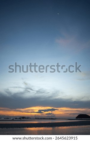 Dramatic twilight sky over the beach with crescent moon and fishing boats.