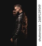 dramatic unshaved man looking to side and adjusting sunglasses while standing in front of black background