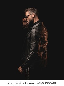 dramatic unshaved man looking to side and adjusting sunglasses while standing in front of black background