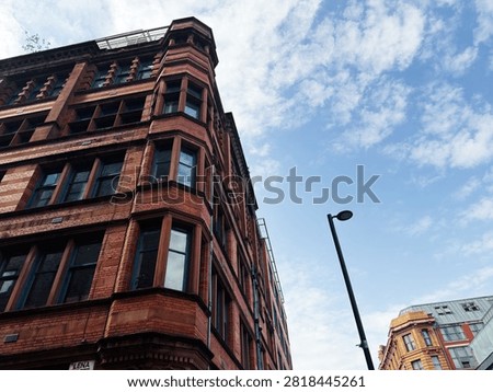 Dramatic upward perspective of a red brick Victorian building in Manchester, UK against a bright sky.