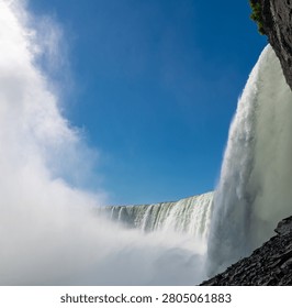 Dramatic Upward View From Behind Niagara Horseshoe Falls With Mist and Blue Sky