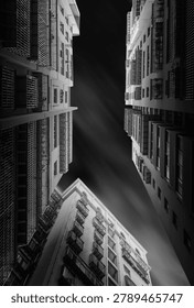 Dramatic upward view between tall urban buildings with balconies and geometric facades under a dark sky.