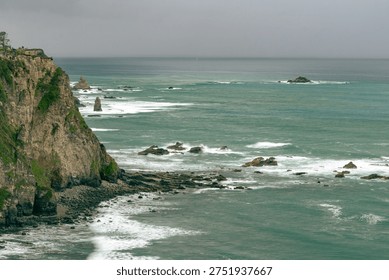 Dramatic vertical cliffs of Costa del Silencio with turquoise ocean waves crashing on rocky shores under a misty sky