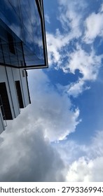 A dramatic vertical low-angle view showing the sharp geometric corner of a modern high-rise building with glass and balconies against a deep blue sky with large cumulus clouds.