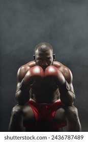 Dramatic vertical portrait of Black muscular boxer looking at camera intensely and wearing red gloves
