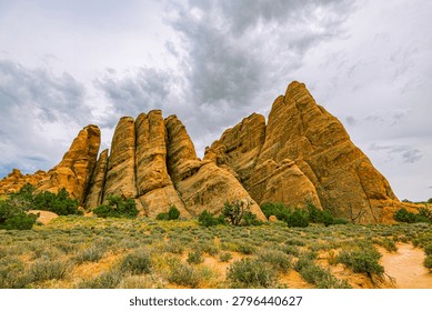 Dramatic vertical sandstone fin formations rise above desert scrub under stormy skies along the Devils Garden trail, Arches National Park, Utah.